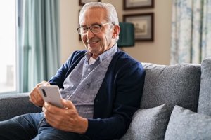 Old man sitting on sofa and making video call with his phone