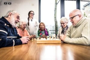 Female caregiver watching senior living citizens playing chess
