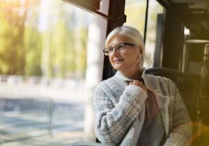 Old woman leaning against the bus window and looking out to the road