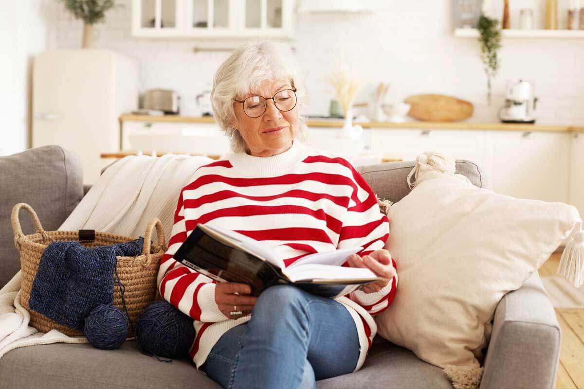 Old woman sitting on the sofa and reading a book