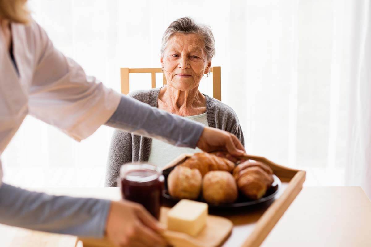 Caregiver prepares breakfast for old woman