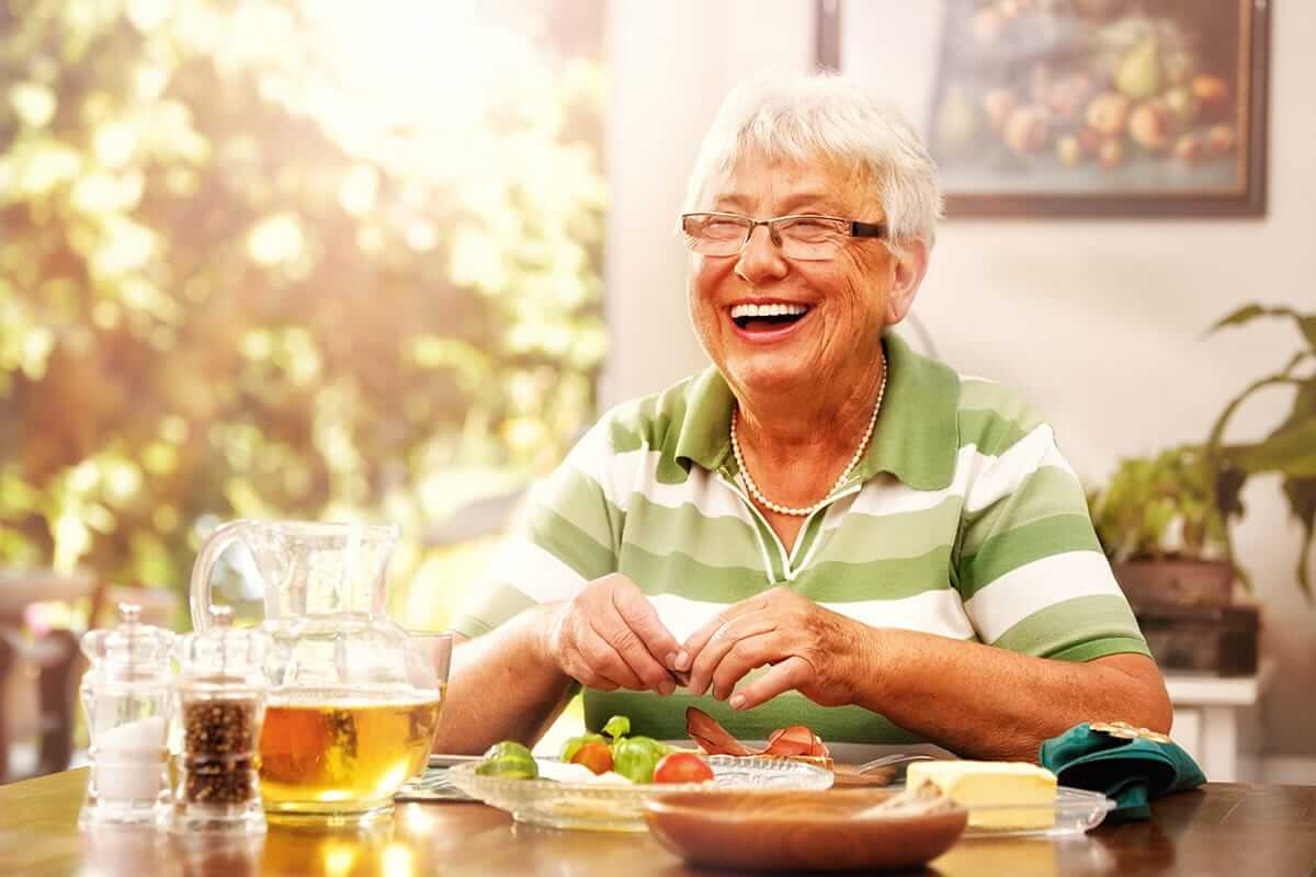 Happy old woman eating some fruit on table