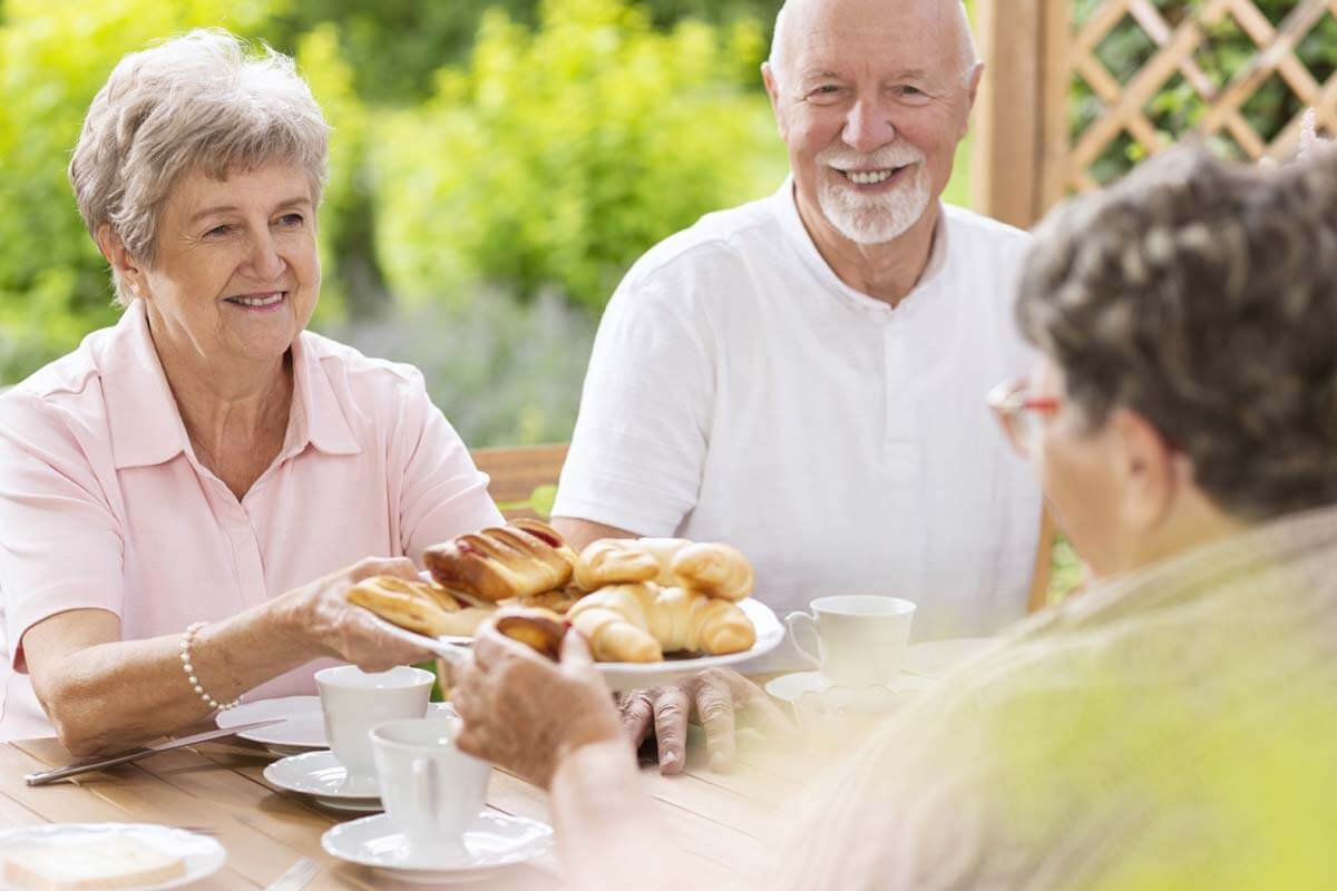 Old woman give a plate of bread to other senior living citizens when lunch