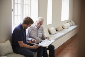 Caregiver helps old man reading a book