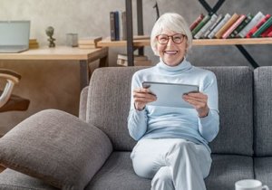 Old woman sitting on sofa and playing her ipad
