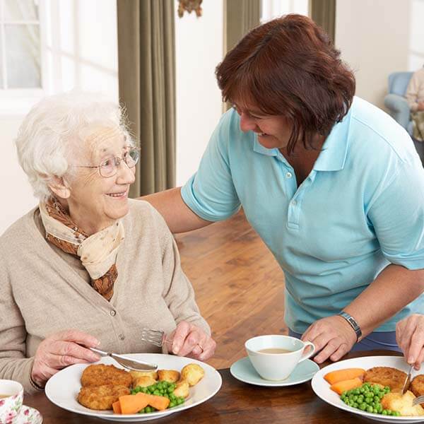 Caregiver help old woman eat her food at lunch